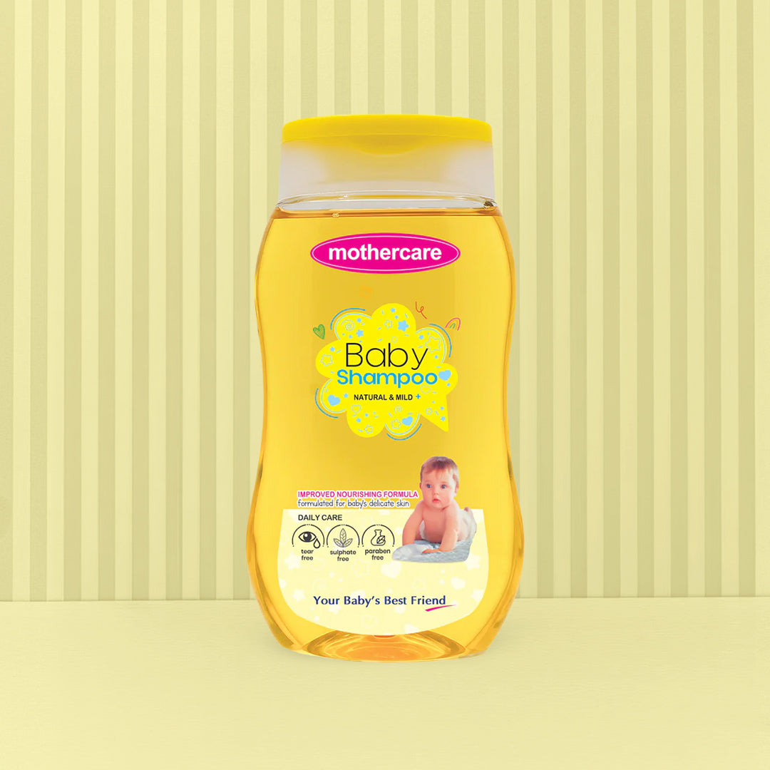 A bottle of Mothercare Baby Shampoo Natural & Mild sulphate free, paraben free, and contains no harmful chemicals centered against a light yellow background with vertical stripes.