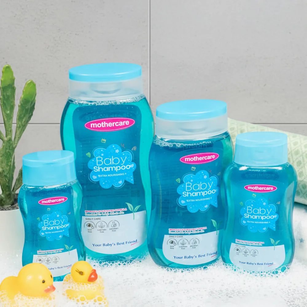 Four bottles of Mothercare Baby Shampoo Tear Free Extra Nourishing in various sizes from small to family sizes, arranged in a bath setting with soap bubbles, rubber ducks, and a small plant.